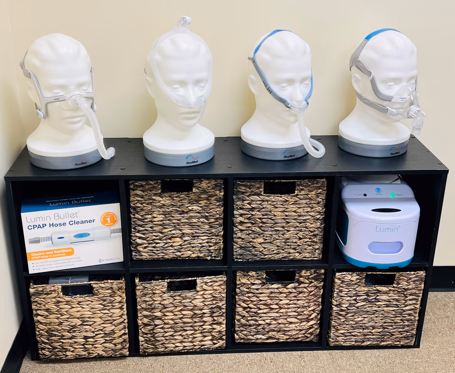 Four CPAP masks on mannequin heads atop a cubby shelf with woven baskets.