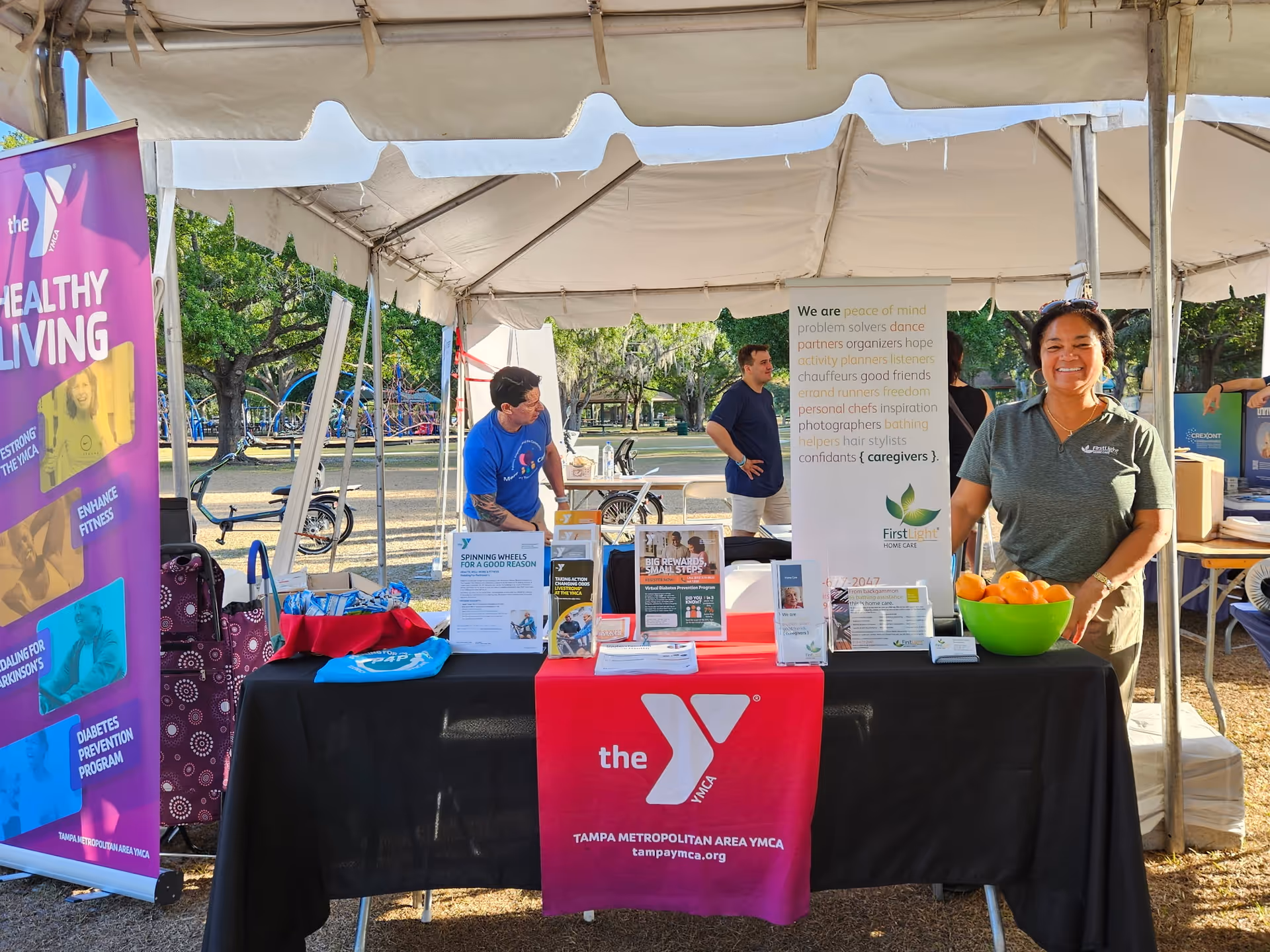 Outdoor tent booth for FirstLight Home Care with smiling staff at a community event.