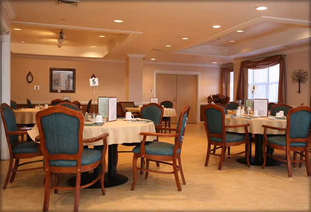 Senior living dining room with round tables and green upholstered chairs.