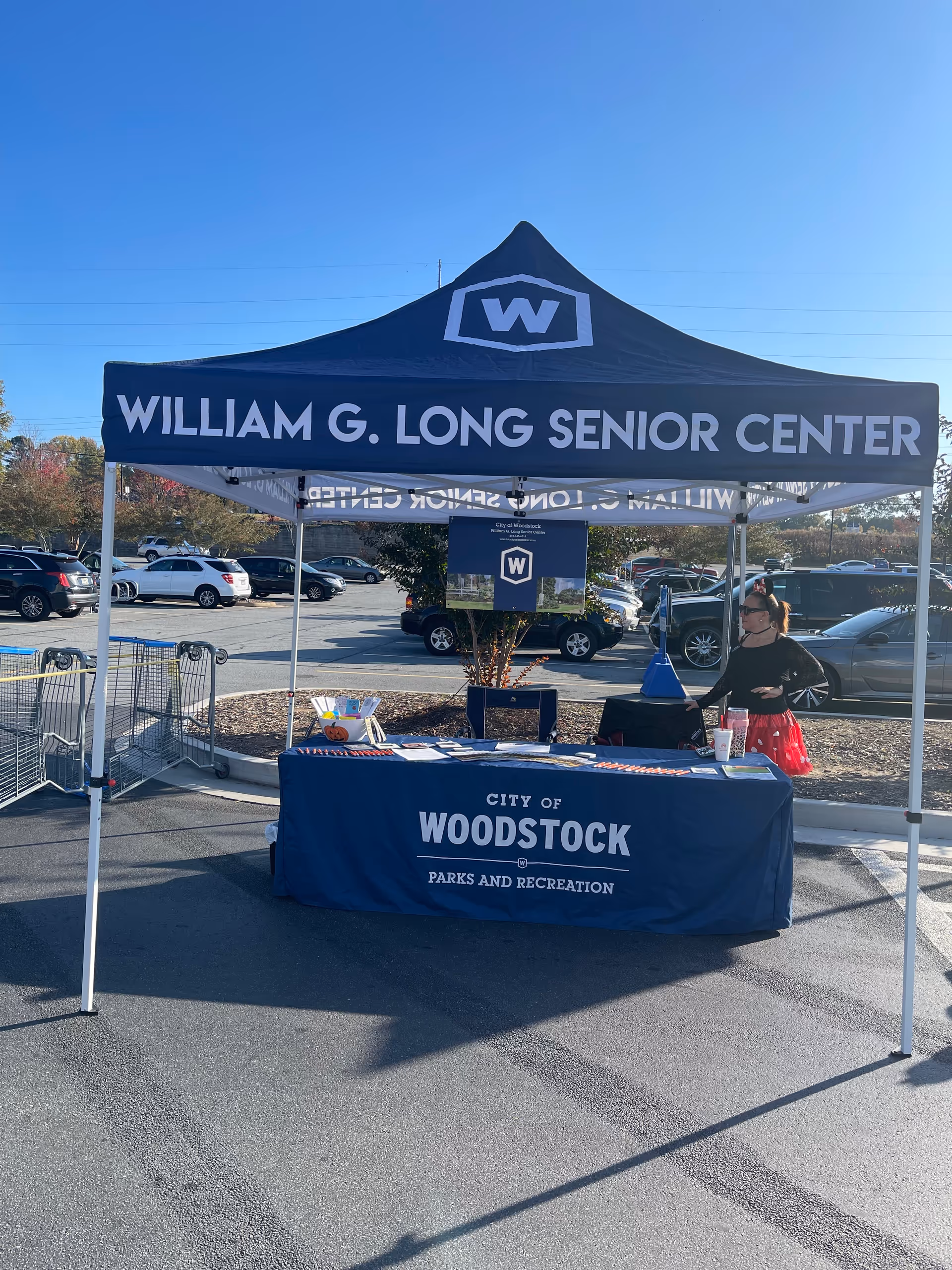 Outdoor event tent with William G. Long Senior Center banner in a parking lot.