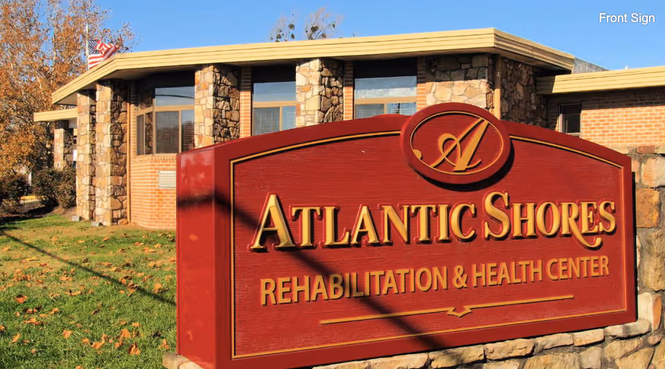 Red entrance sign reading "Atlantic Shores Rehabilitation & Health Center" in front of a stone-faced building and lawn.