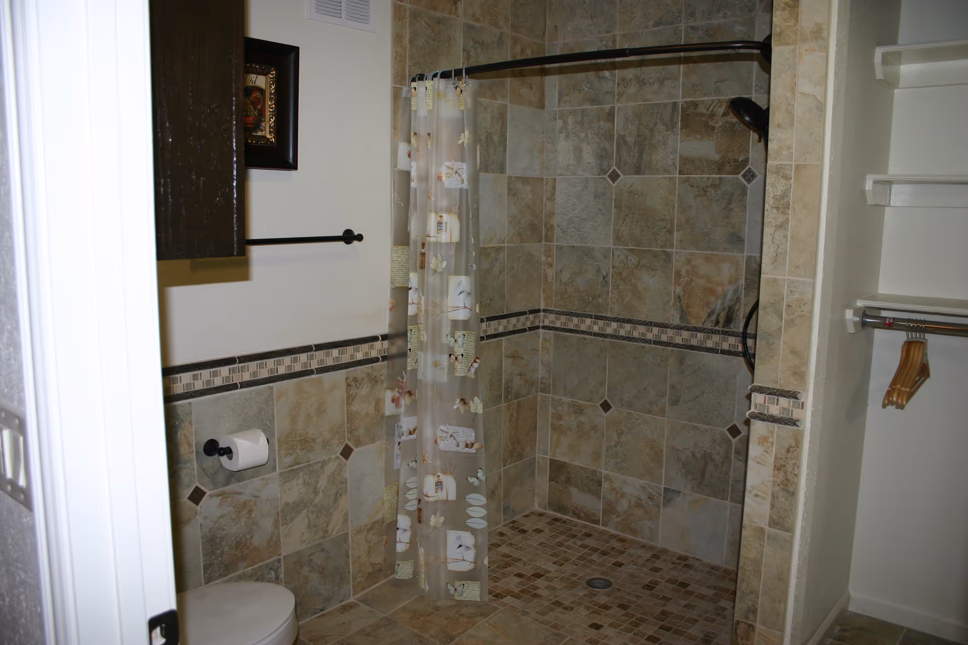 Beige-tiled bathroom with a corner shower, shower curtain, toilet, and built-in shelves.