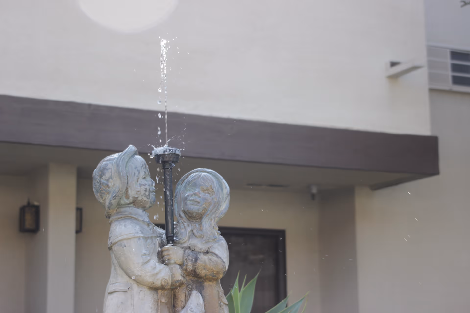 Outdoor fountain statue of two figures holding a lamp near the entrance.