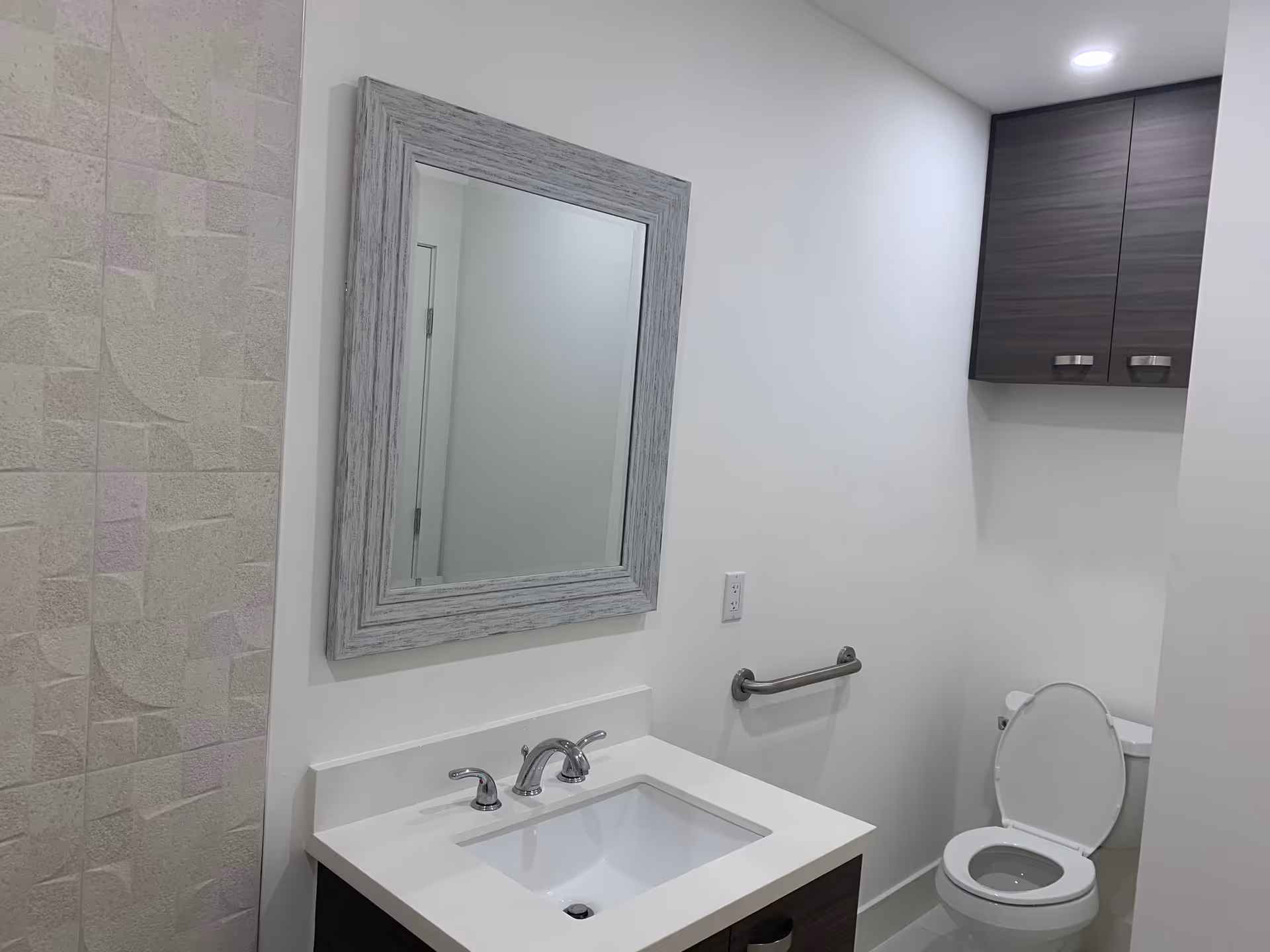 Modern bathroom with sink, mirror, toilet, and wall cabinet.