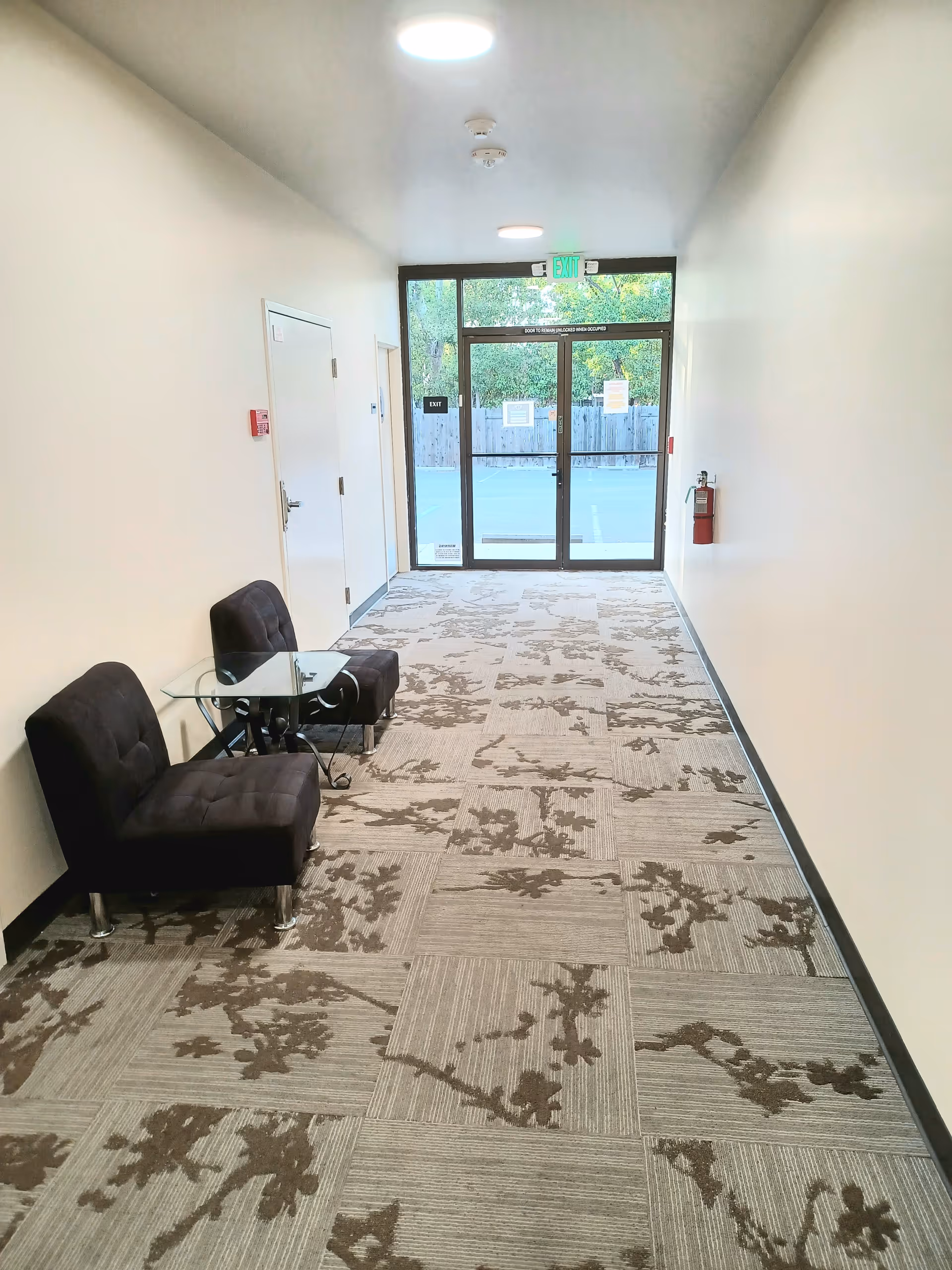 Narrow hallway with two black upholstered chairs and a glass table near the entrance