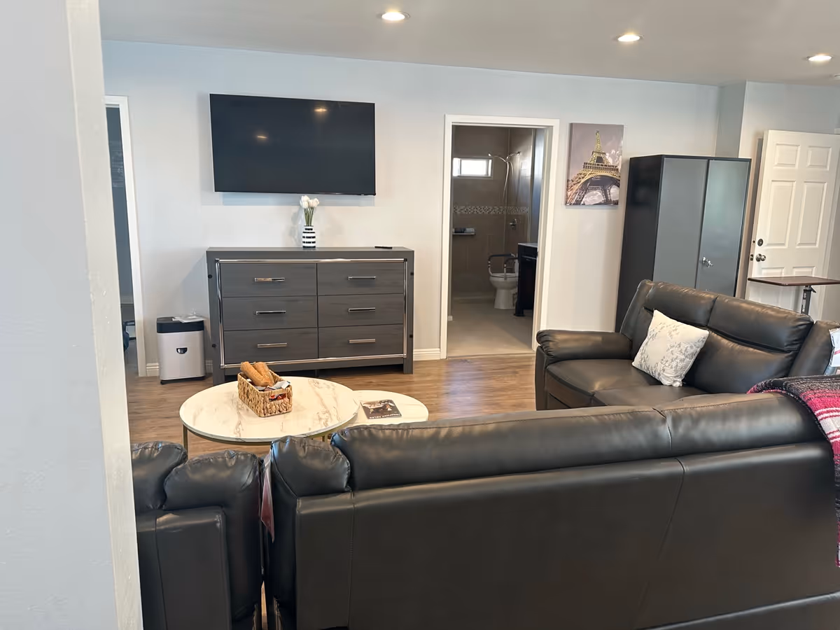 Living room with black leather sofas, coffee table, TV, dresser, and bathroom doorway in a suite.