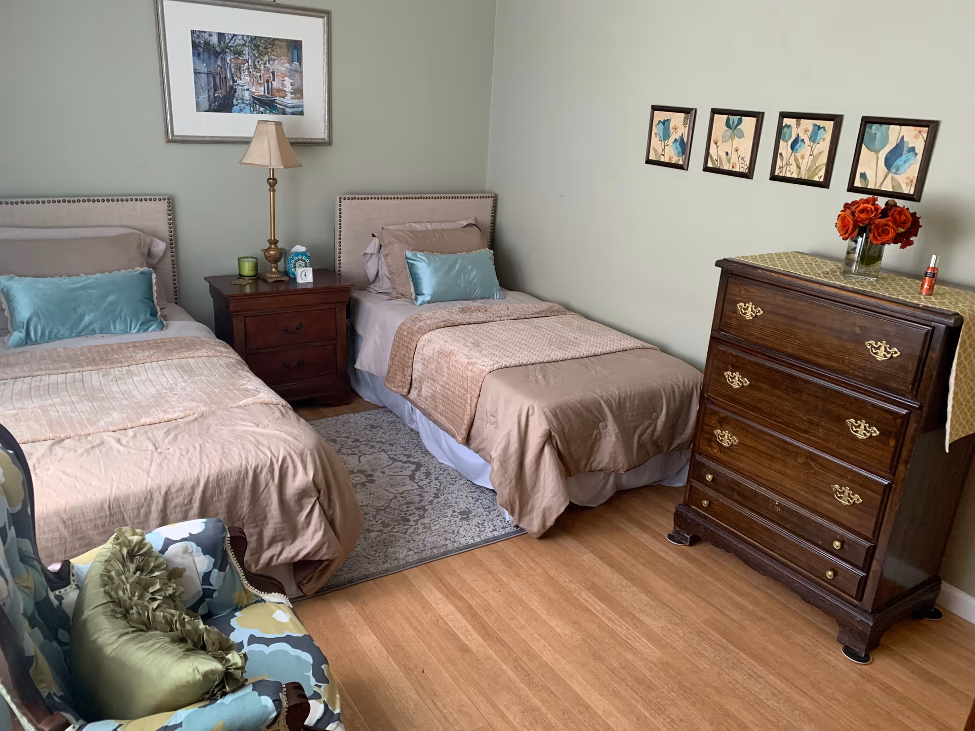 A shared bedroom with two twin beds, beige bedding, teal accent pillows, and a dresser.