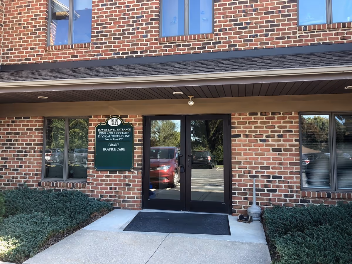Brick building with glass doors and a green Grane Hospice Care sign at the entrance.