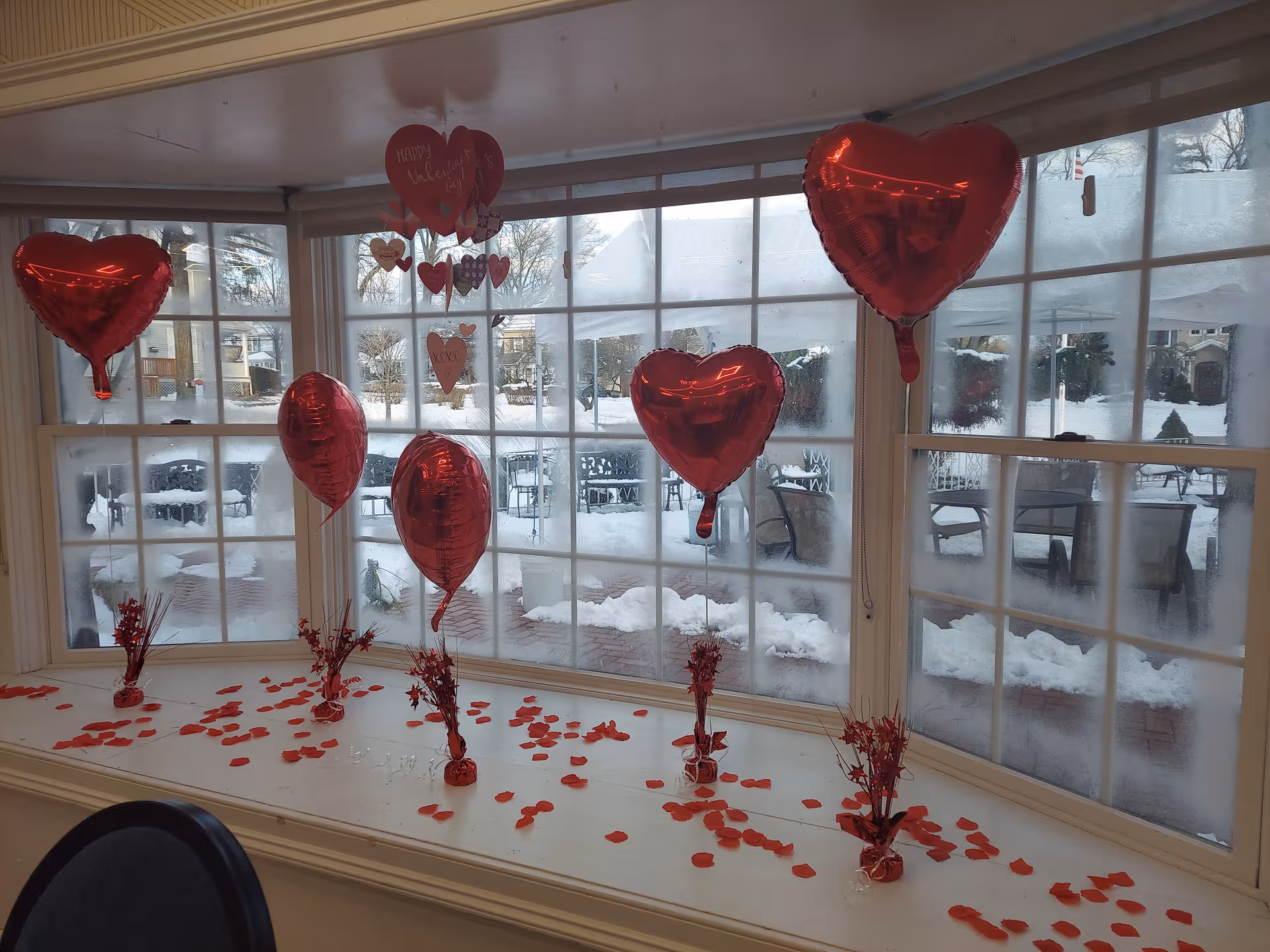 Valentine-themed red heart balloons decorate a sunlit interior windowsill.