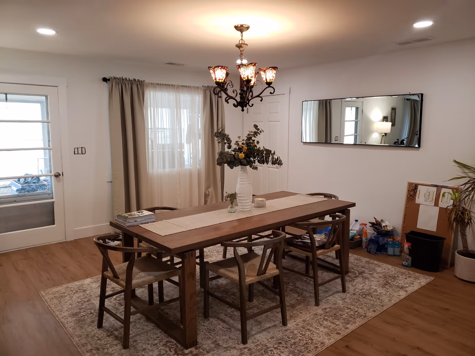 Bright dining room with a long wooden table, chairs, chandelier, and centerpiece.