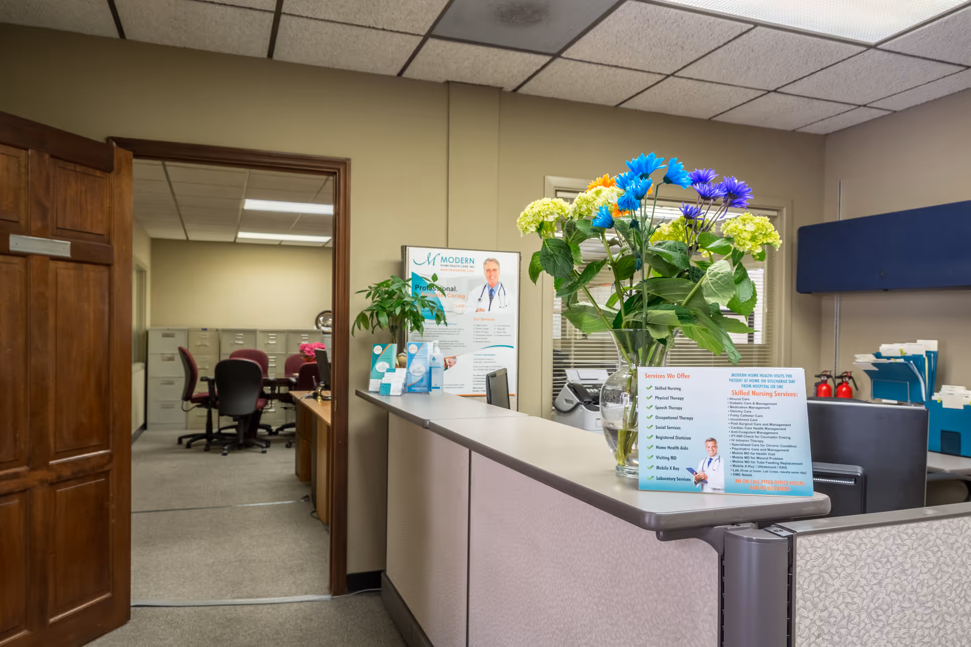 Reception desk in a senior care facility lobby with flowers, brochures, and posters.