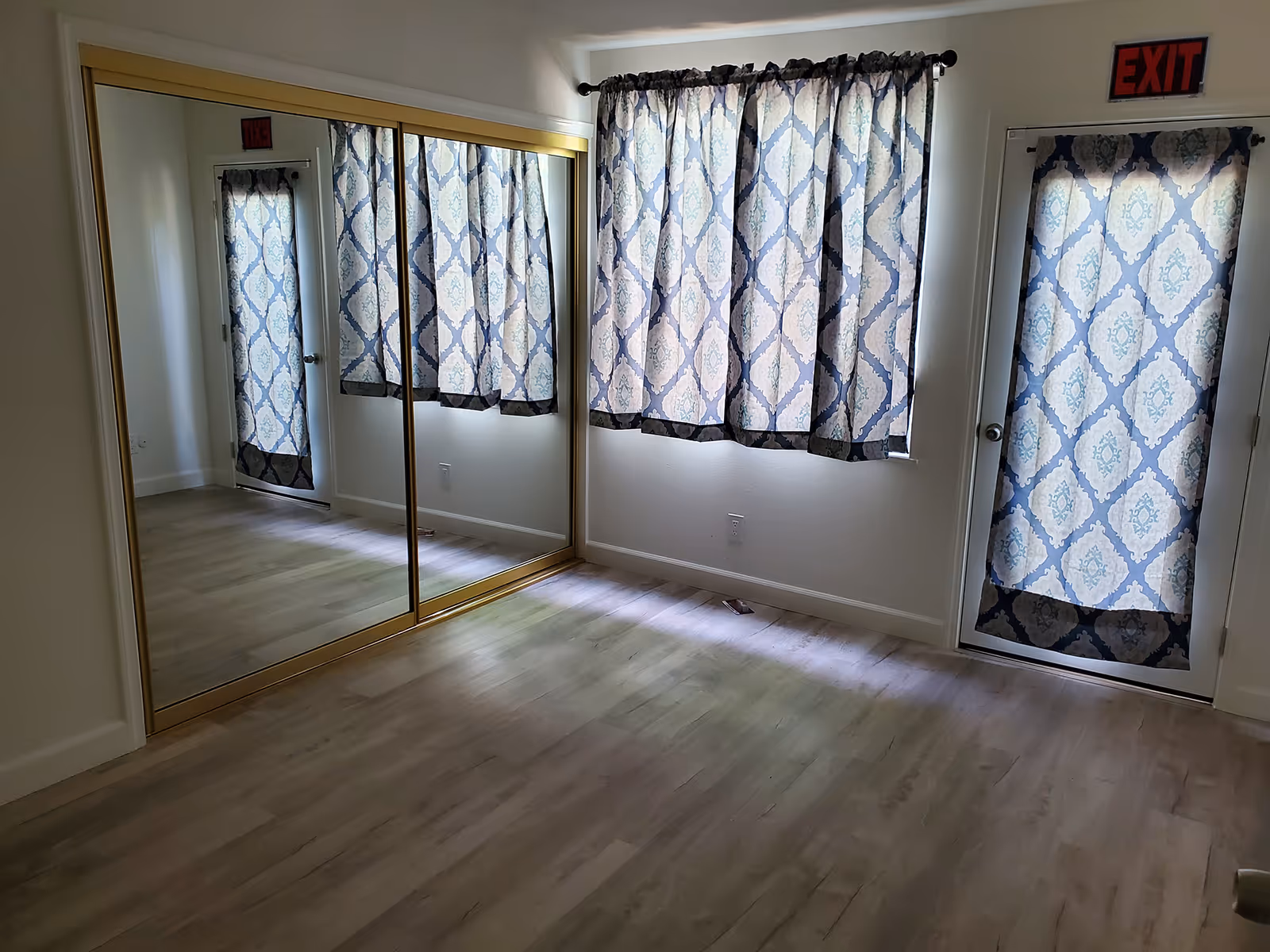 A bright bedroom with a large mirrored closet and blue patterned curtains.