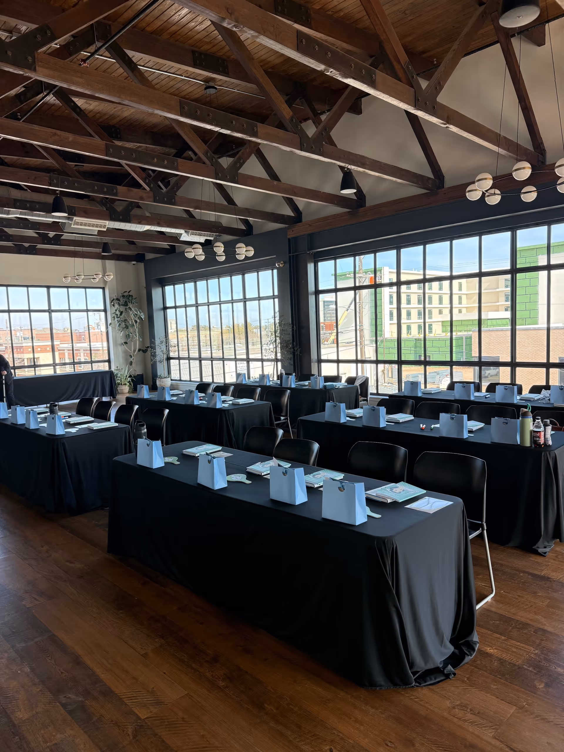 Sunlit conference room with long black-cloth tables, blue gift bags, and expansive windows.