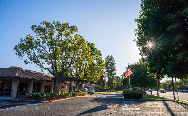 Senior living facility exterior with parking lot, trees, and an American flag.