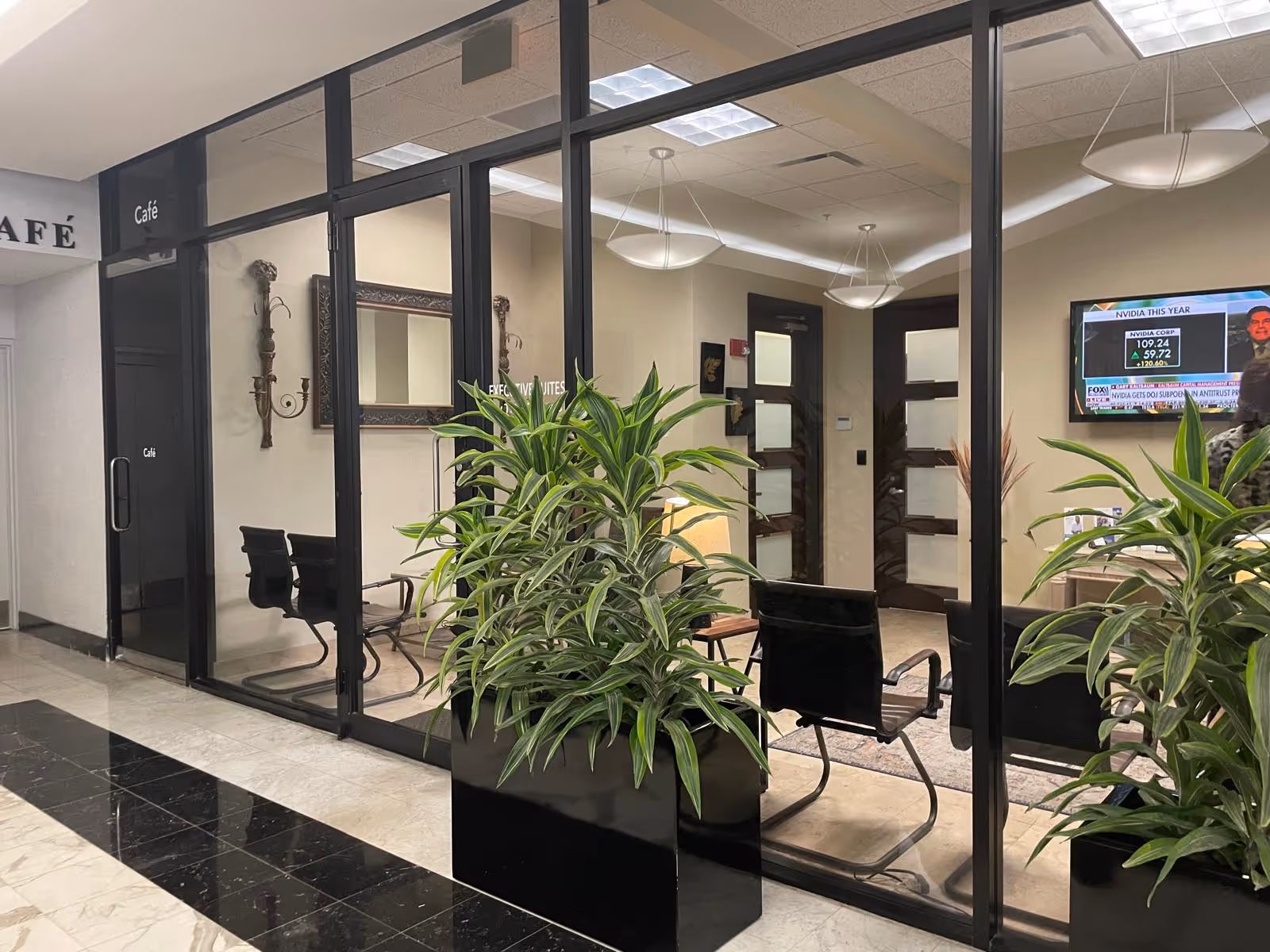 Lobby area with glass partition, seating, and tall potted plants.