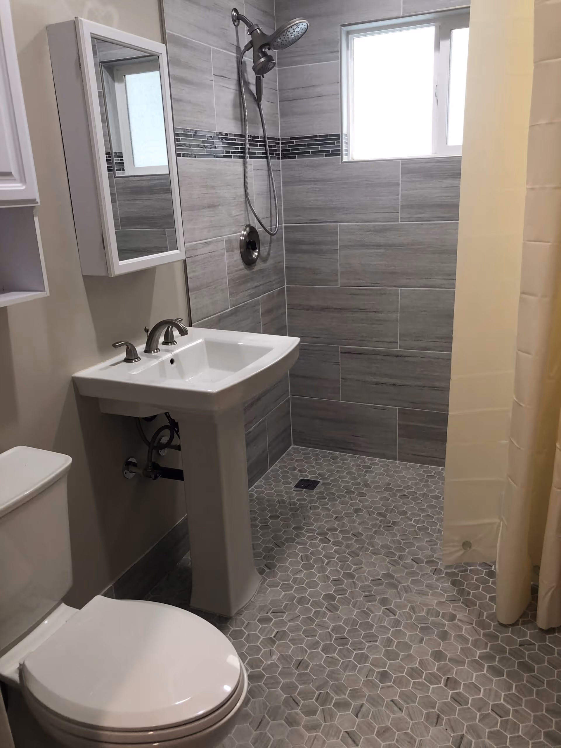 Modern bathroom featuring a pedestal sink, toilet, and tiled walk-in shower.