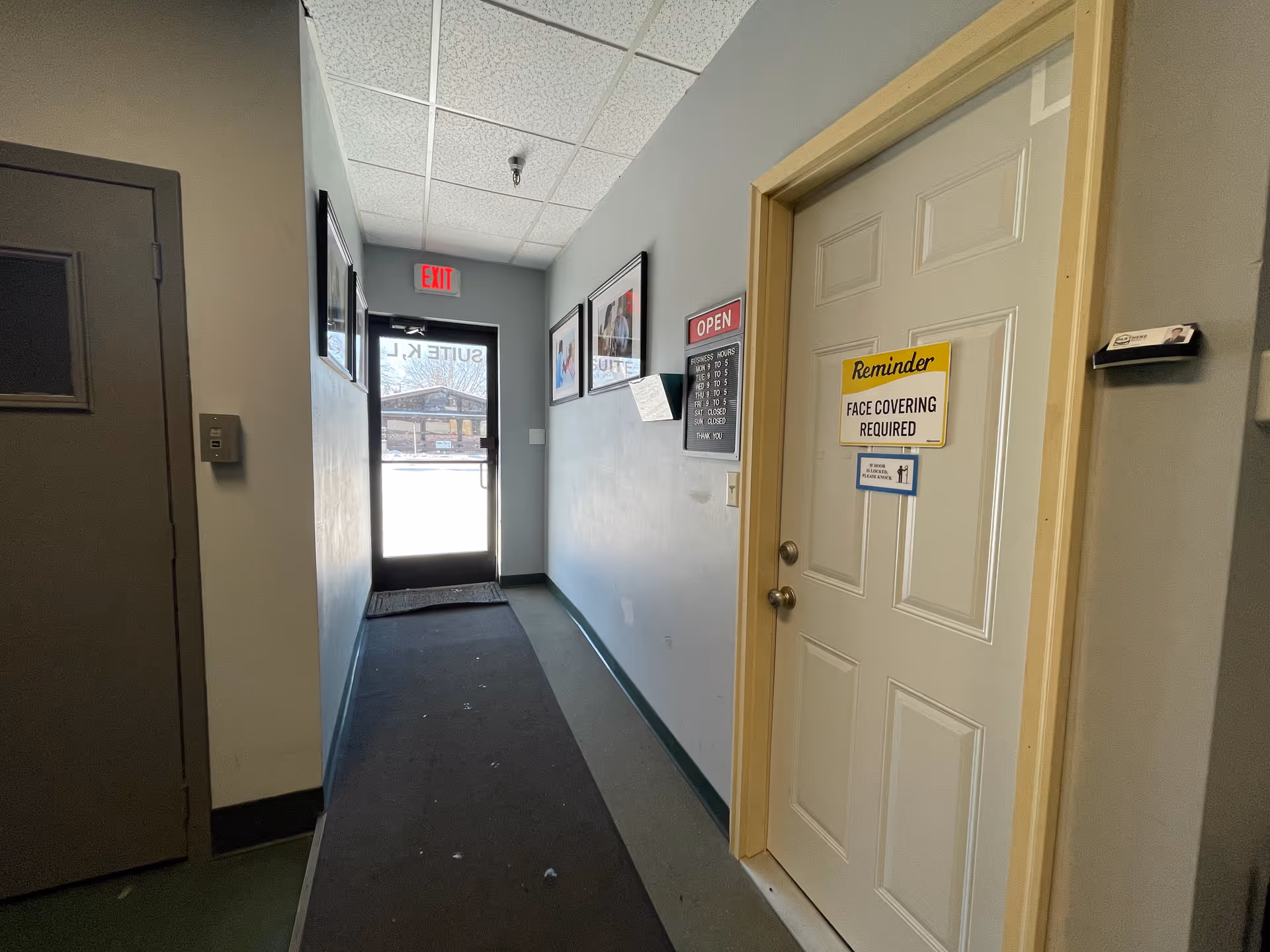 Narrow interior hallway with an exit door, signs, and a closed door on the right.