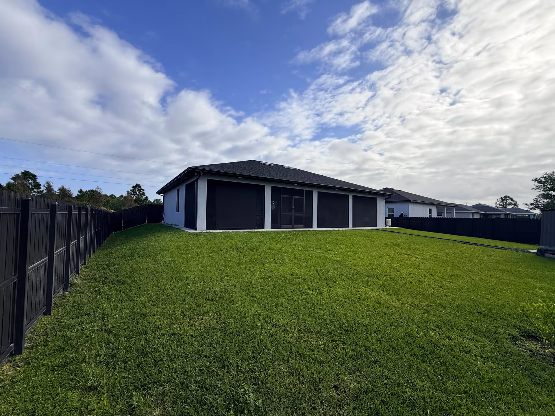 A single-story building with a large grassy yard and dark privacy fencing.