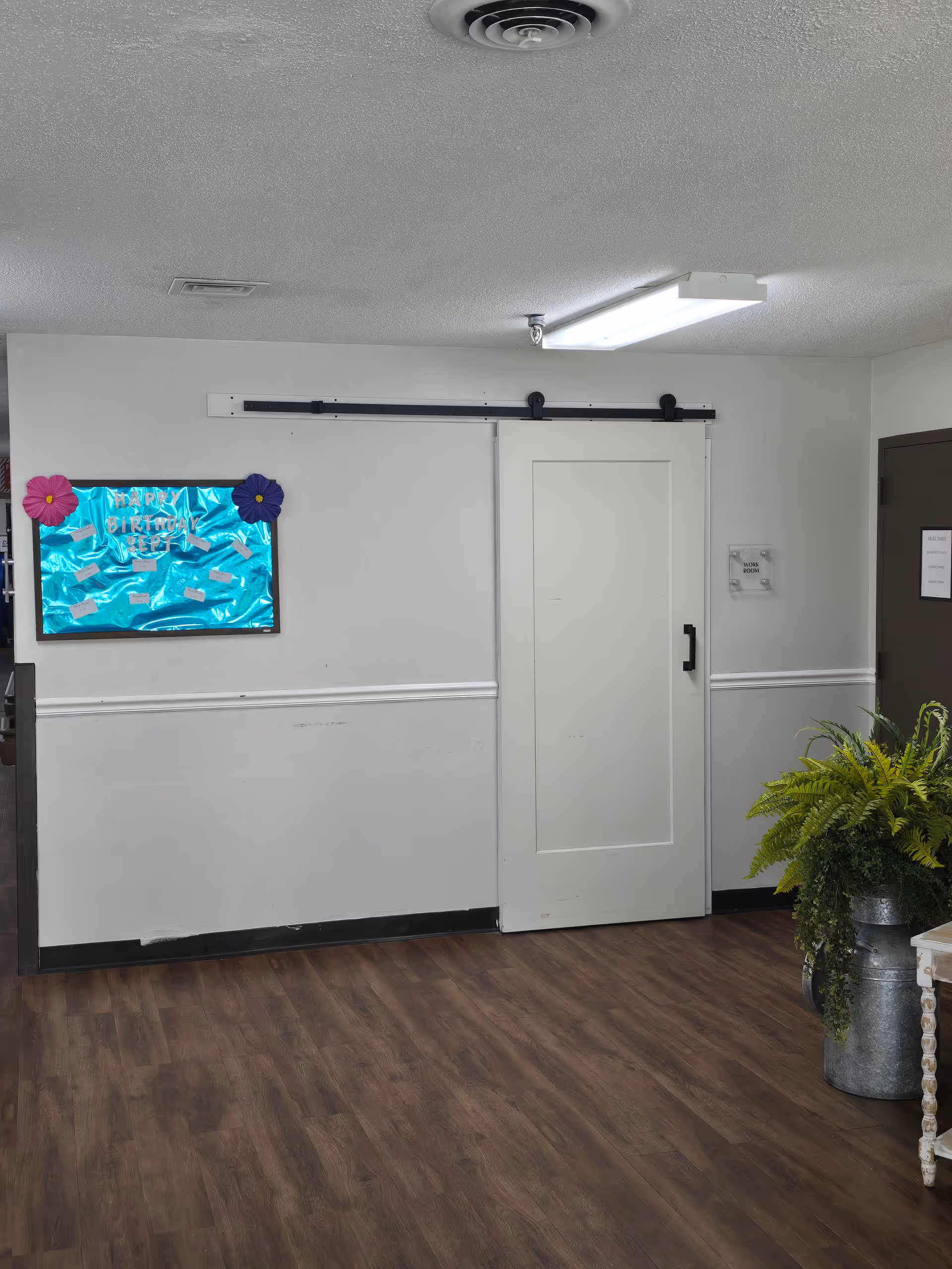 Interior hallway featuring a white sliding barn-style door, bulletin board, and potted fern.