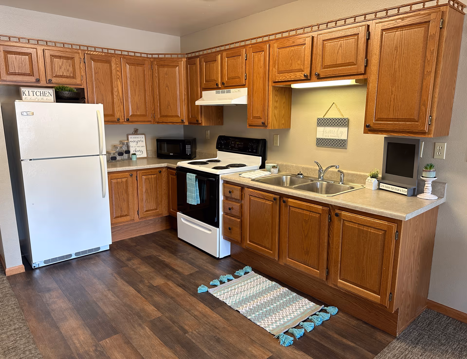 A compact kitchen with wooden cabinets, a white refrigerator, stove, sink, and decor.