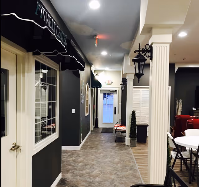 A hallway inside Arbor Rose of Tolono with dark walls, seating, and decorative columns.