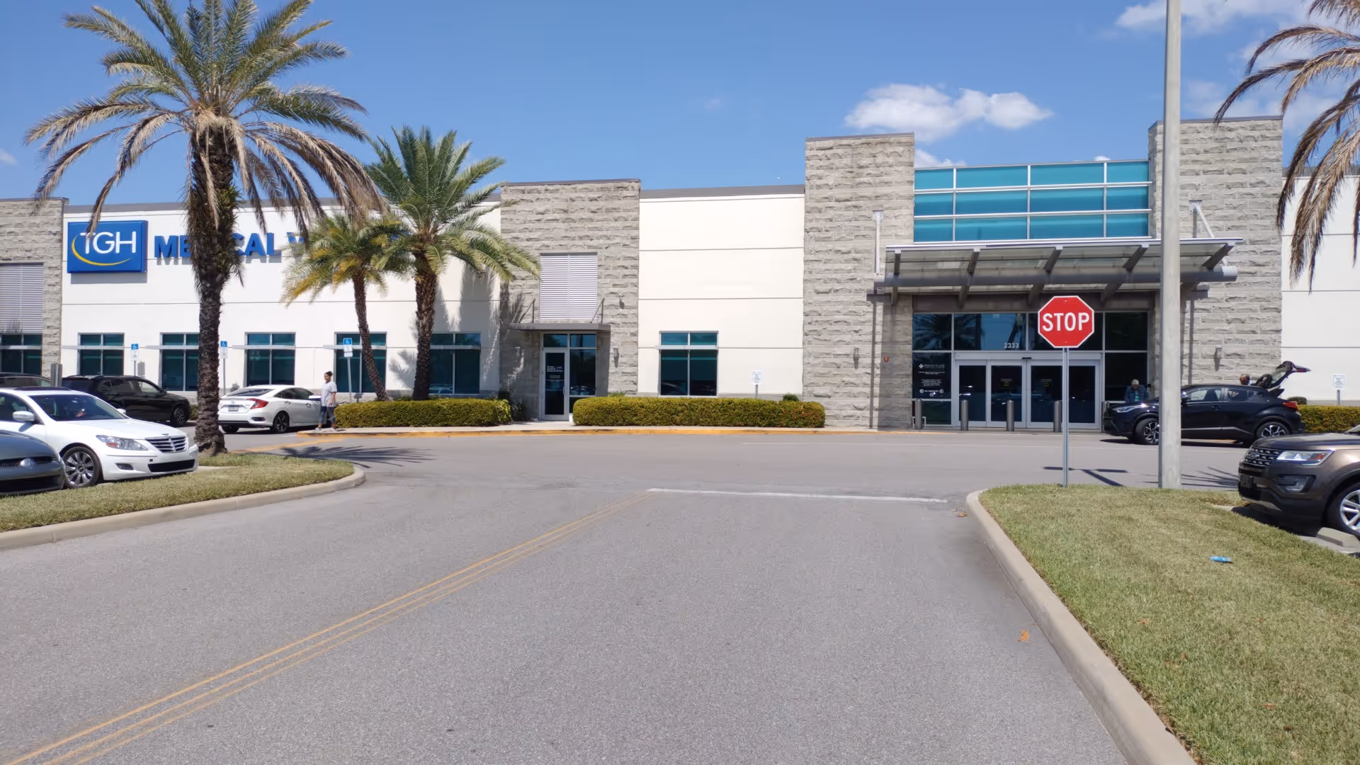 Exterior view of a modern medical facility with palm trees and a parking lot.