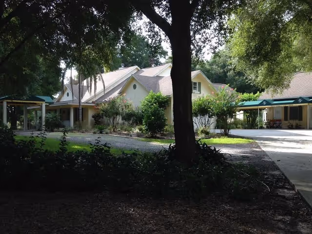 Exterior view of a senior living facility with trees and a walkway.