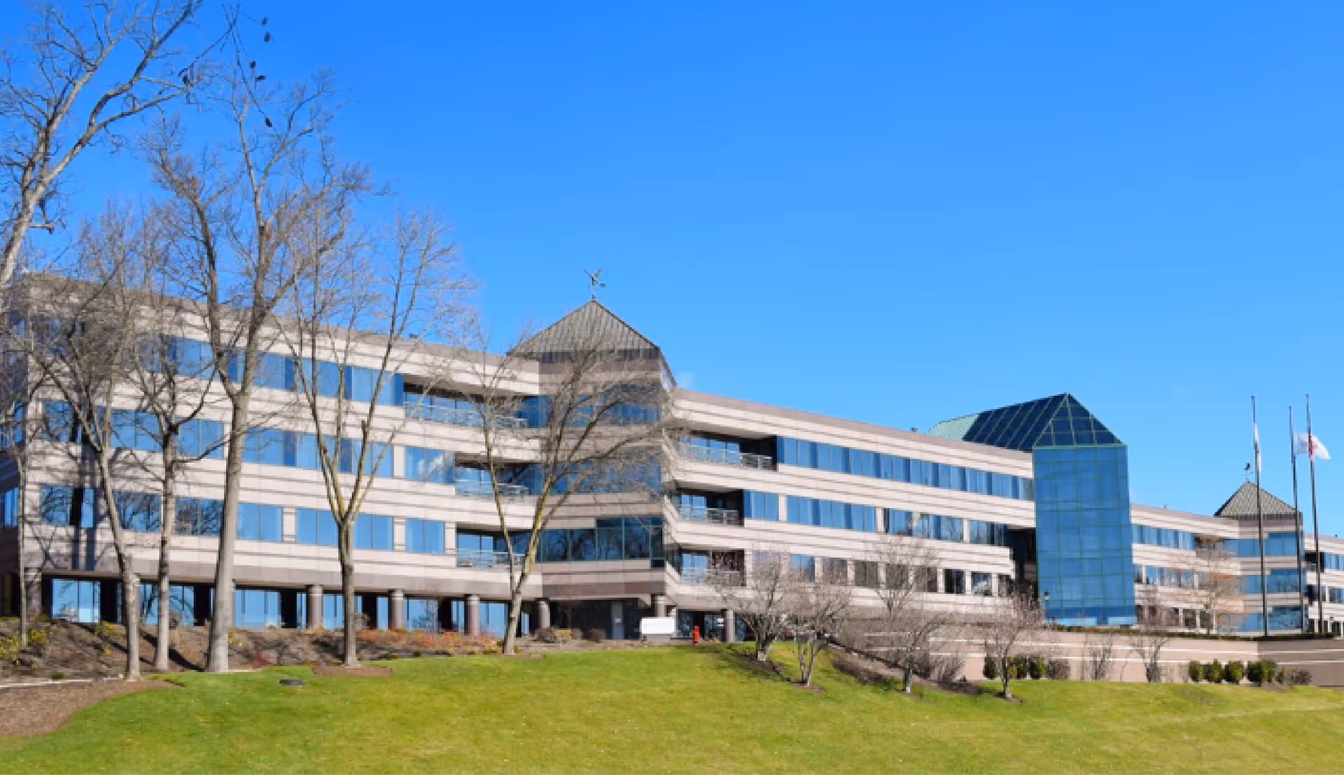 Large modern multi-story facility exterior with glass facade, trees, and blue sky.