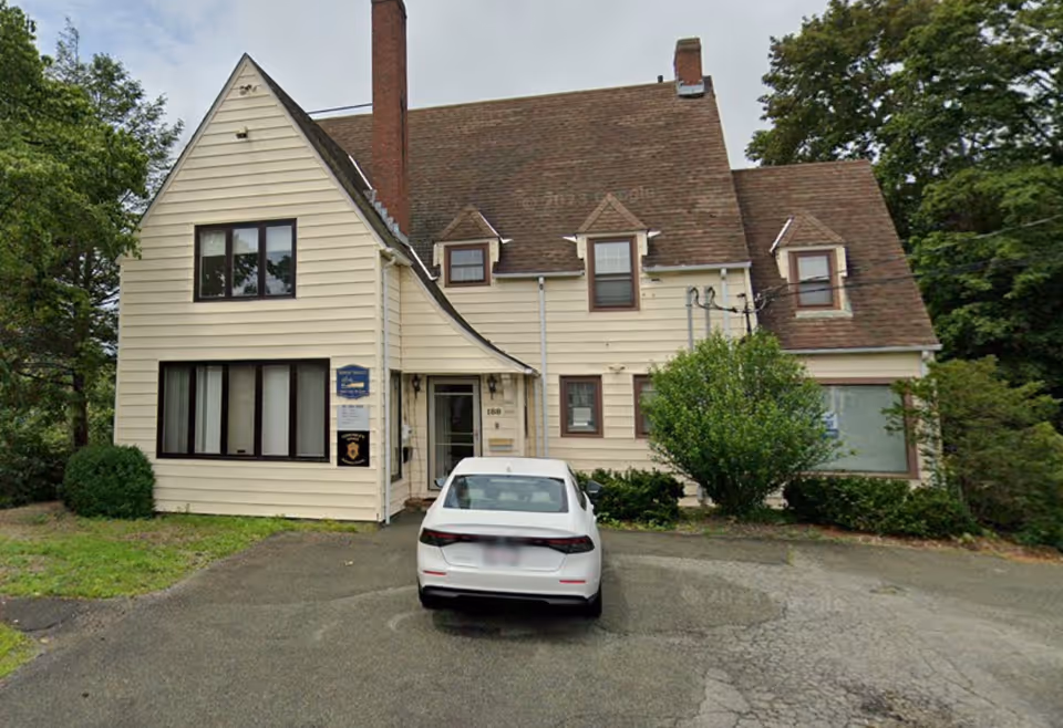 Two-story beige building with a white car parked in a curved driveway.