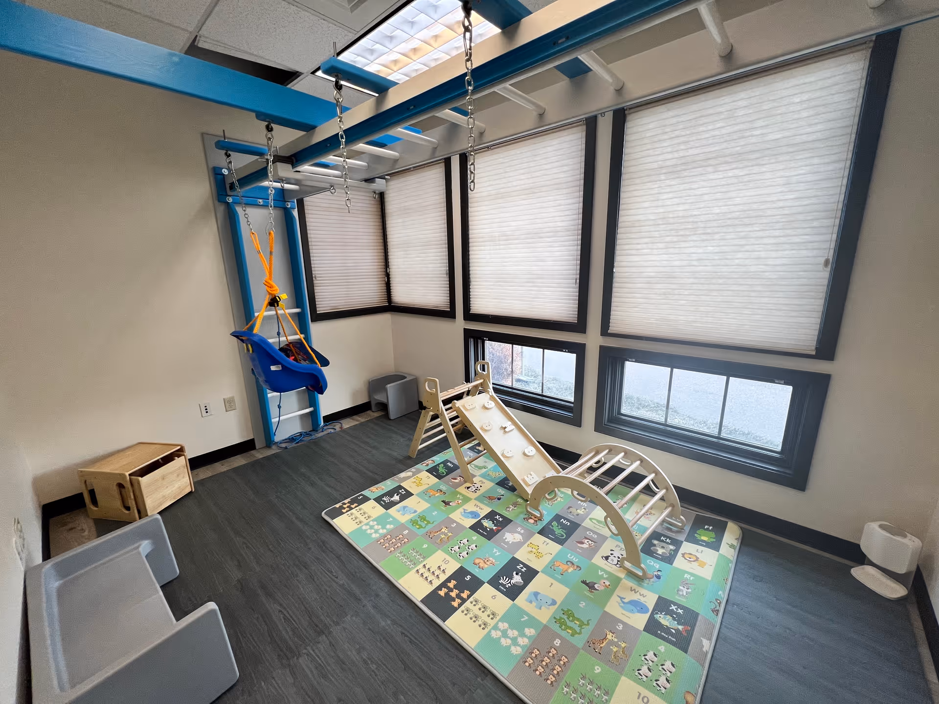 Indoor pediatric play area with a climbing ramp, swing, and colorful foam mat.