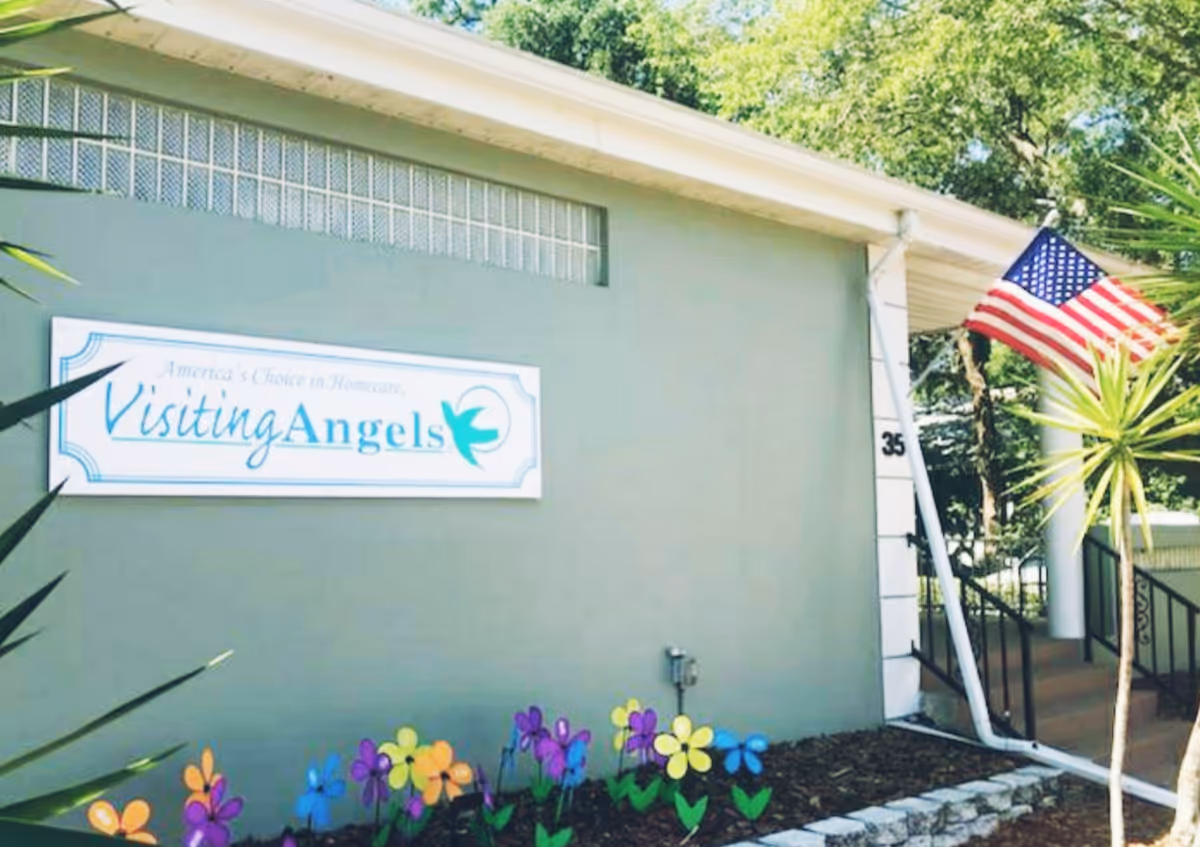 Exterior view of Visiting Angels facility with sign, American flag, and colorful flowers.