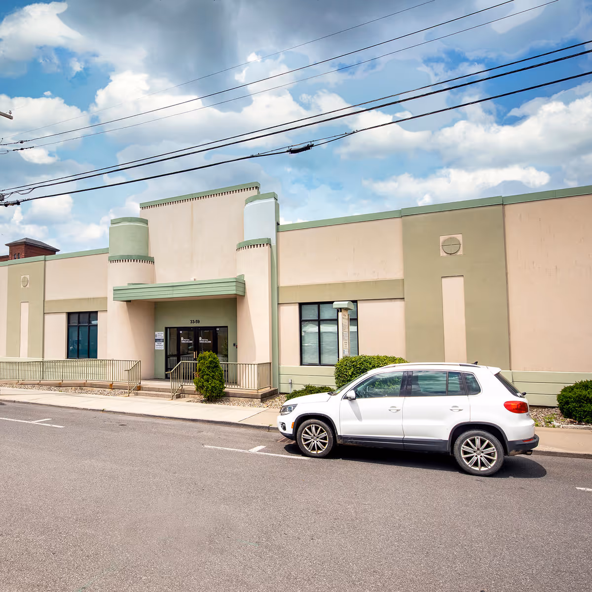 Exterior view of a beige and green medical building with a white SUV parked outside.