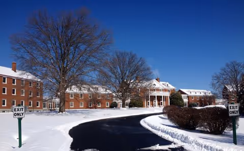 Snowy The Culpeper campus with brick buildings, leafless trees, and a curved road.