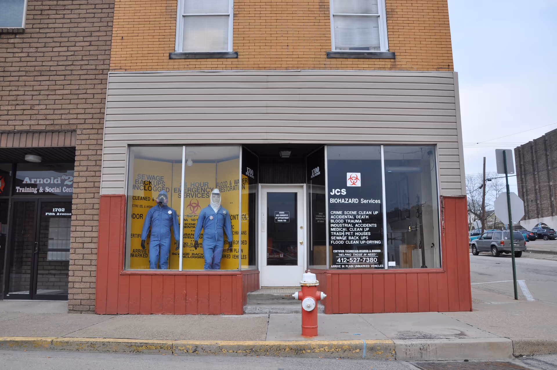 Storefront display with two blue hazmat-suited figures in windows and JCS Biohazard Services sign