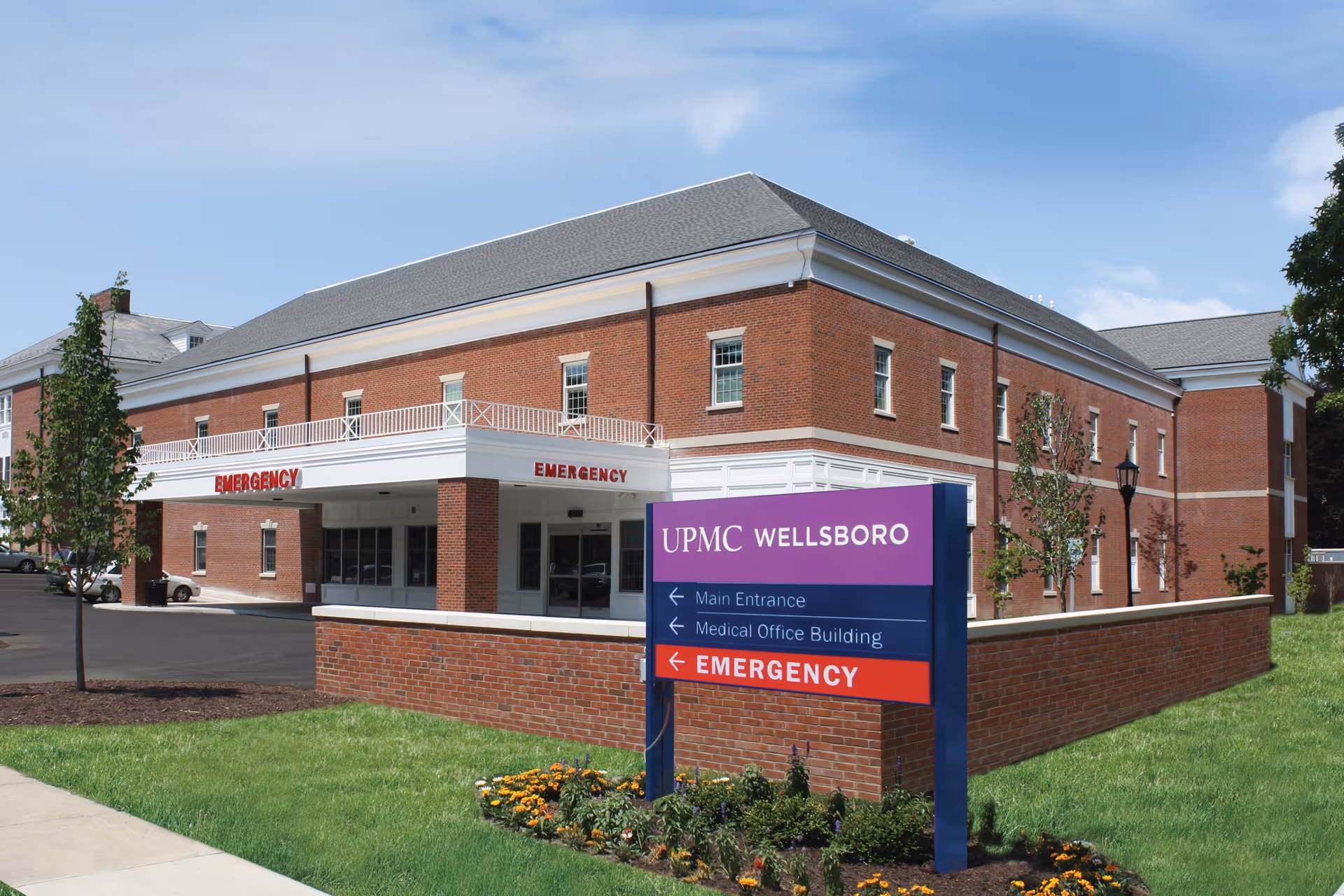 Brick building with emergency entrance and UPMC Wellsboro sign, landscaped lawn in foreground.