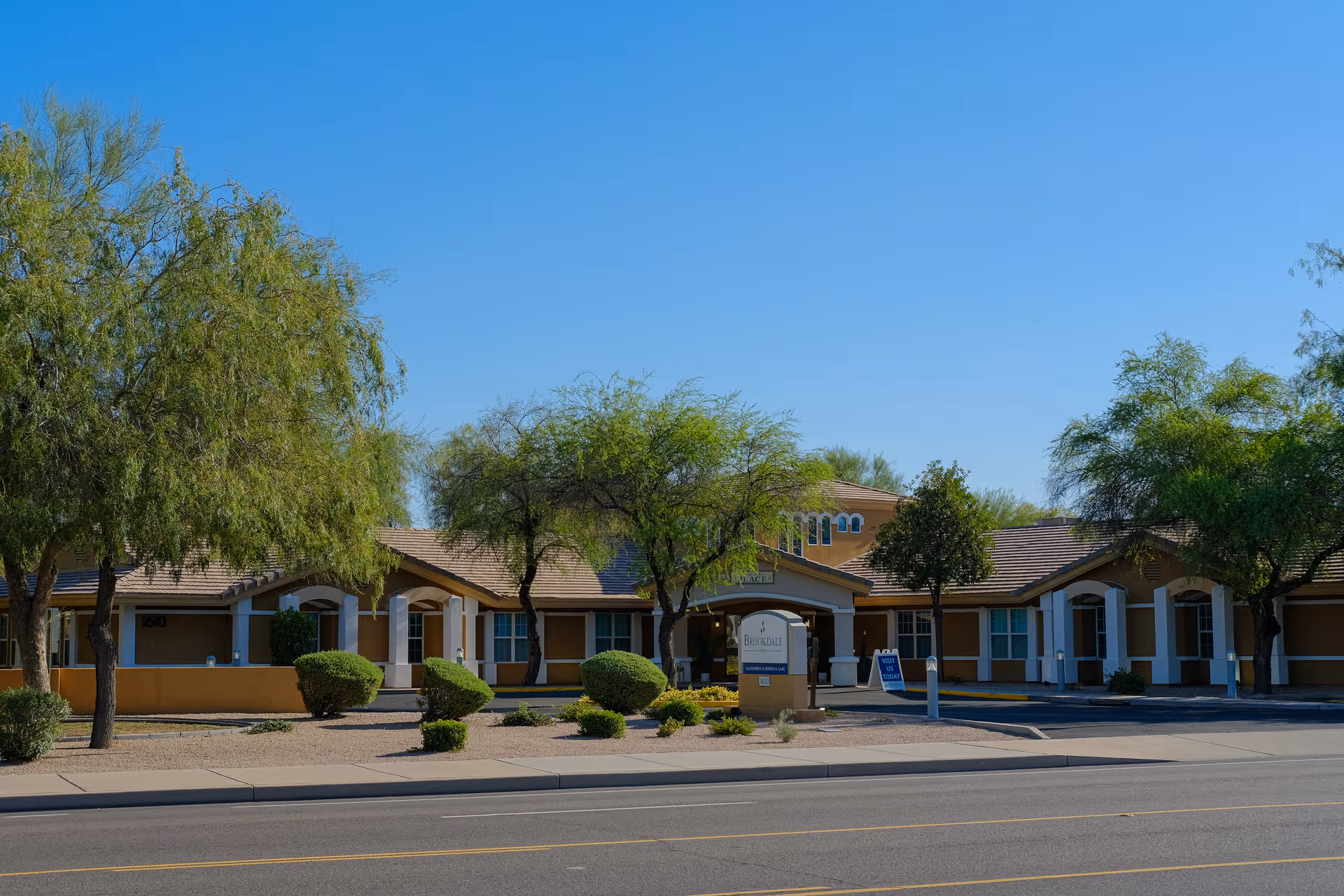Brookdale Tempe exterior: beige single-story building with arches, landscaping, and trees along the street.