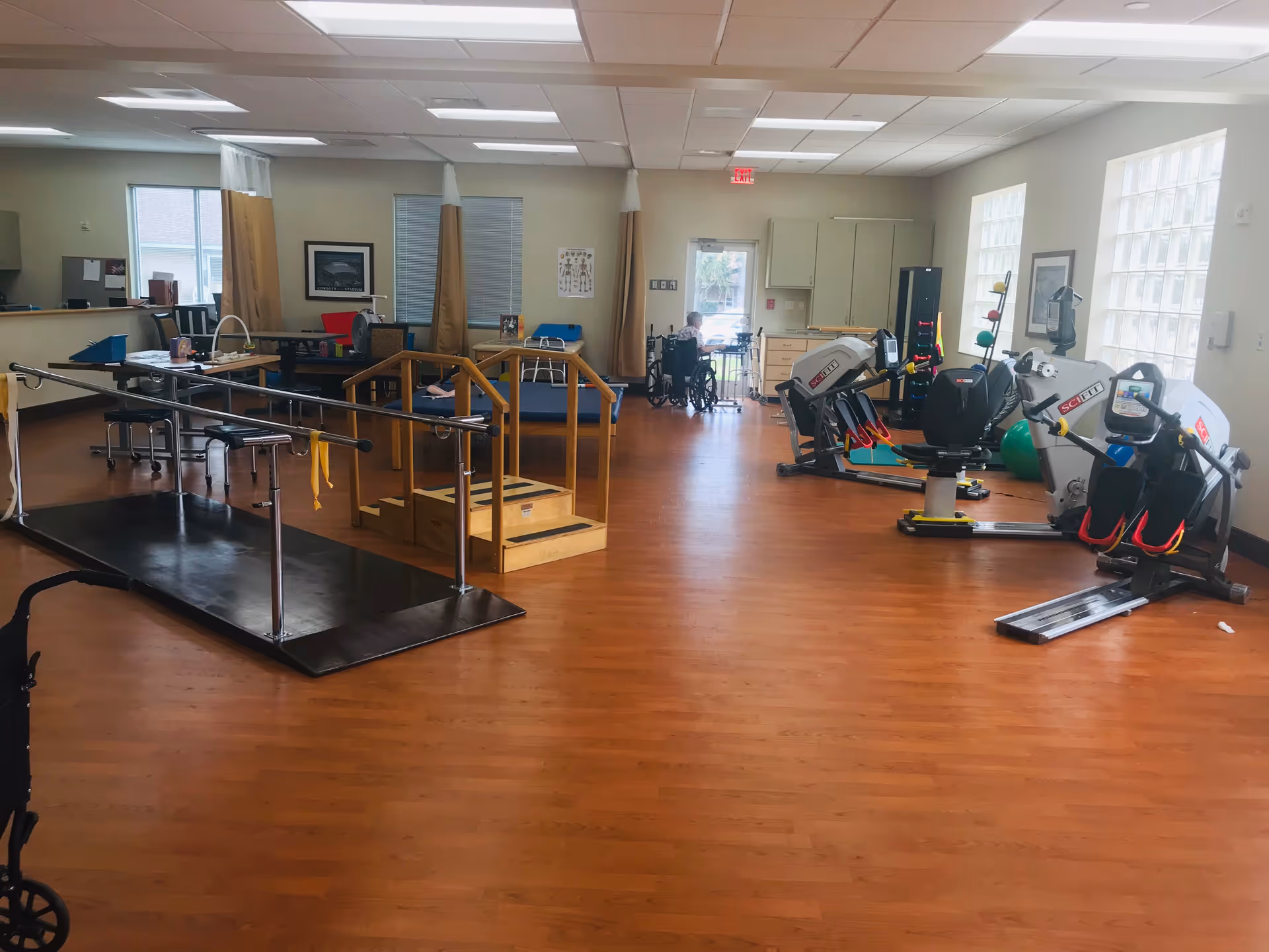 Bright indoor rehab gym at Arlington Villas with parallel bars and exercise equipment.