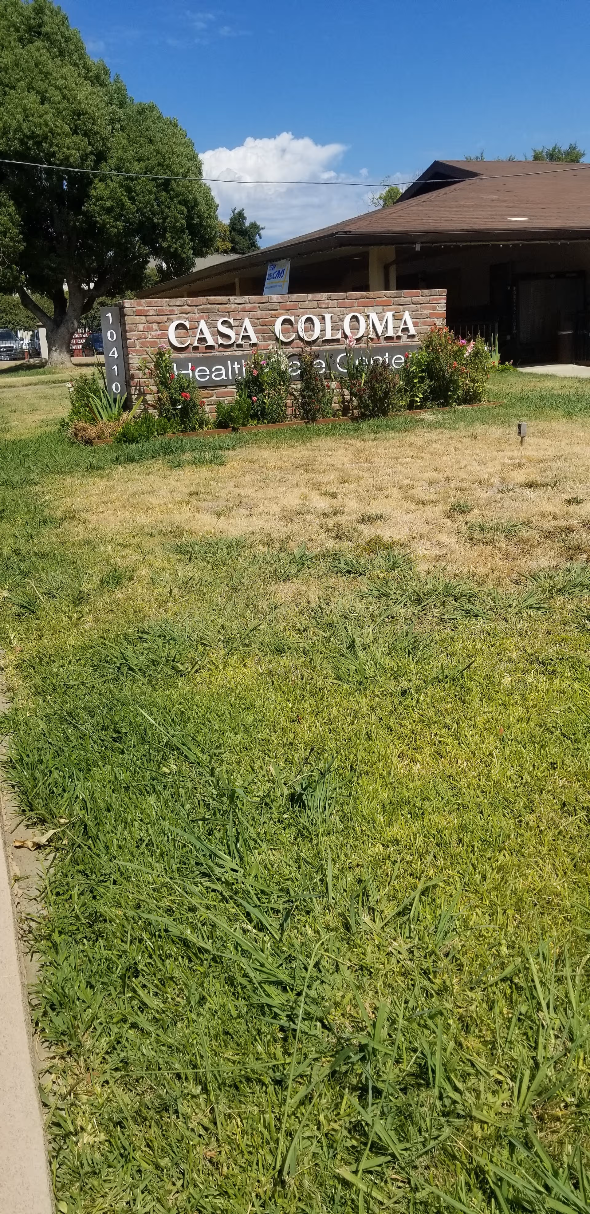 Exterior view of Casa Coloma Health Care Center sign with lawn and trees.