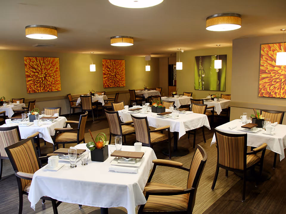 A spacious dining room with white tablecloths, chairs, and colorful wall art.