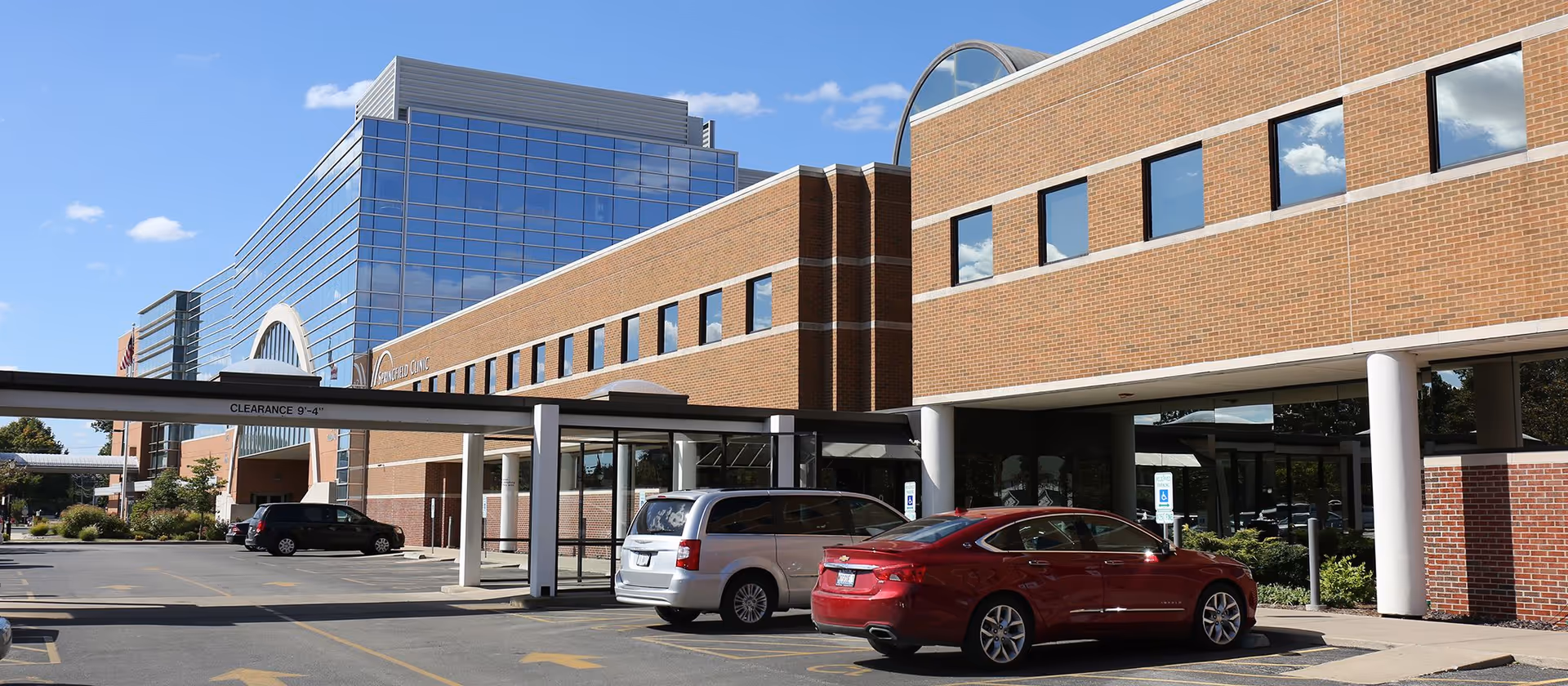 Brick senior living center exterior with covered entry and parked cars.