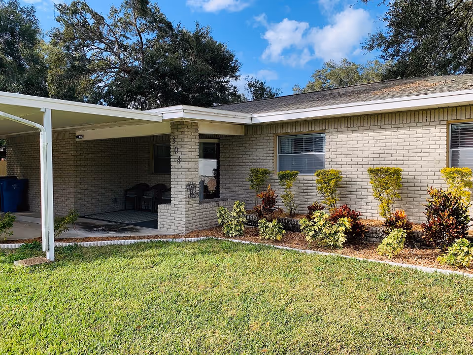Brick single-story building exterior with a covered entrance, window, and landscaped shrubs.