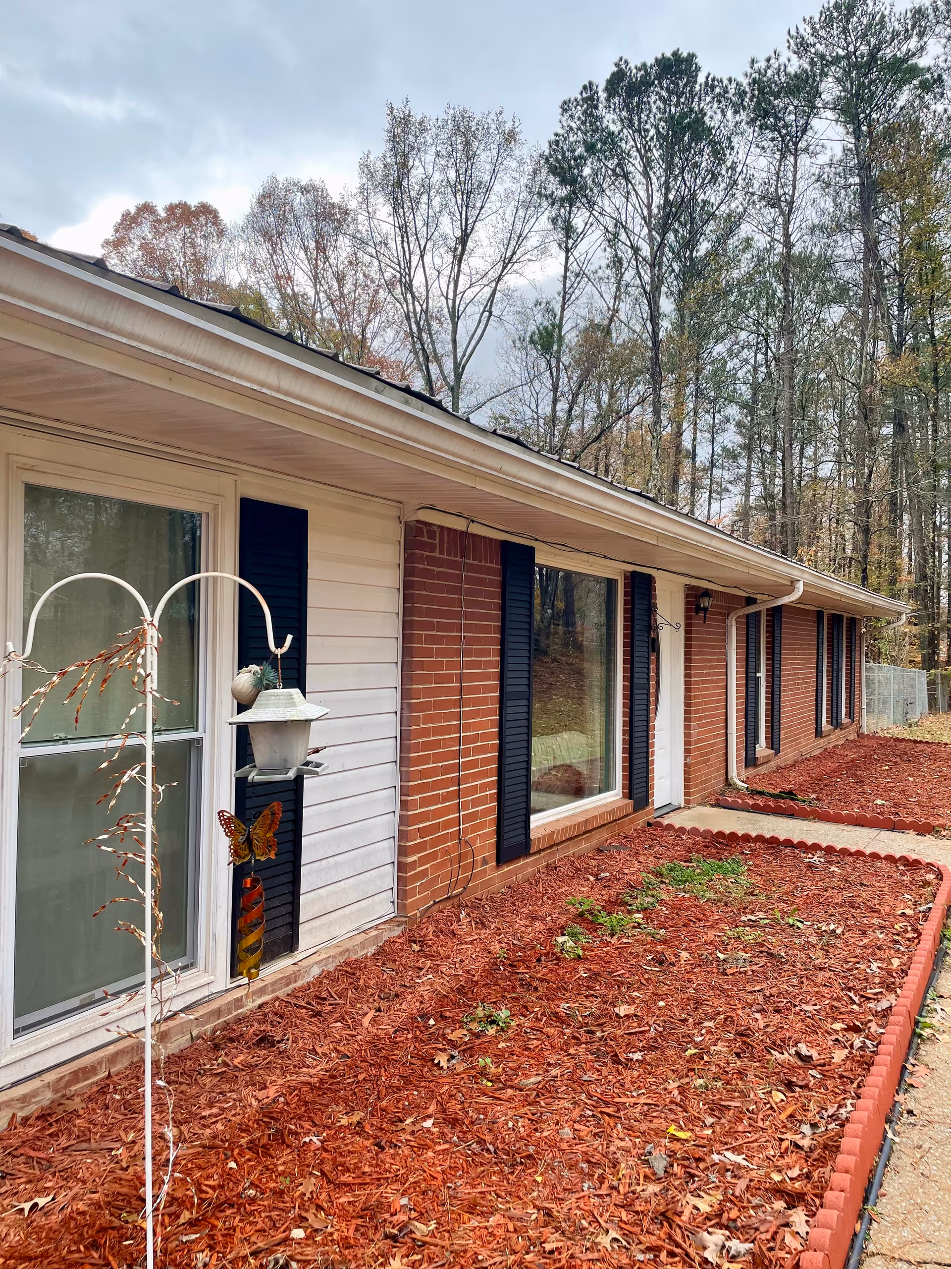 Exterior view of a brick senior living home with windows and red mulch beds.