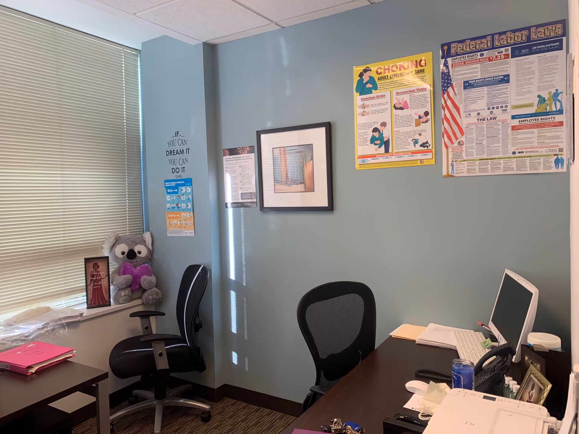 A small office with a desk, computer, and posters on blue walls.