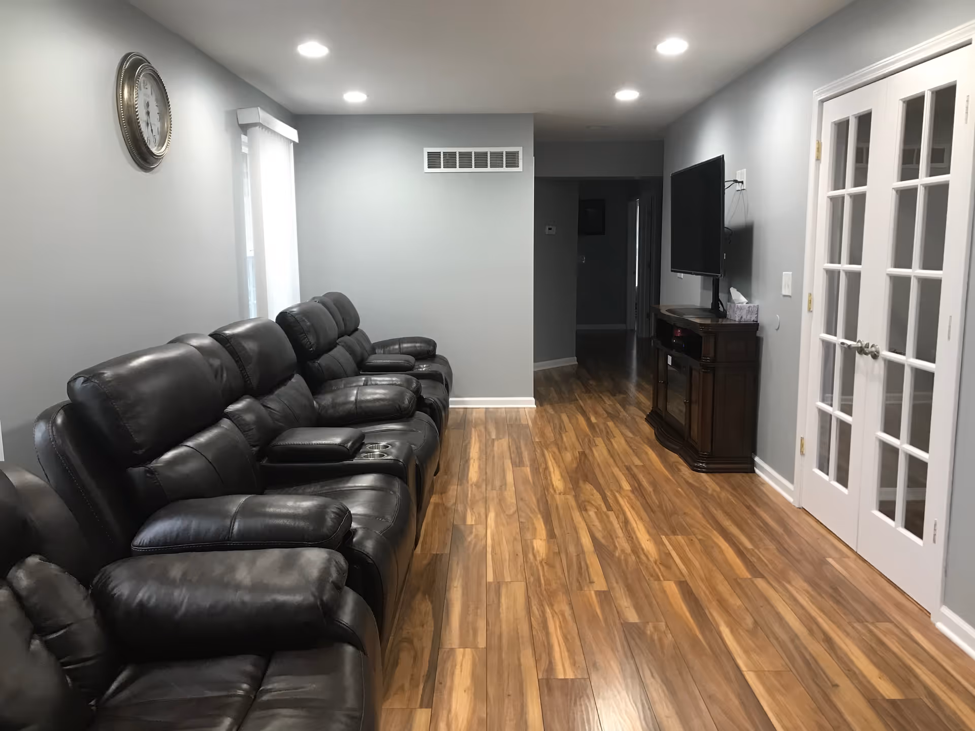 Row of black leather recliners along a gray living room with a wall mounted TV.