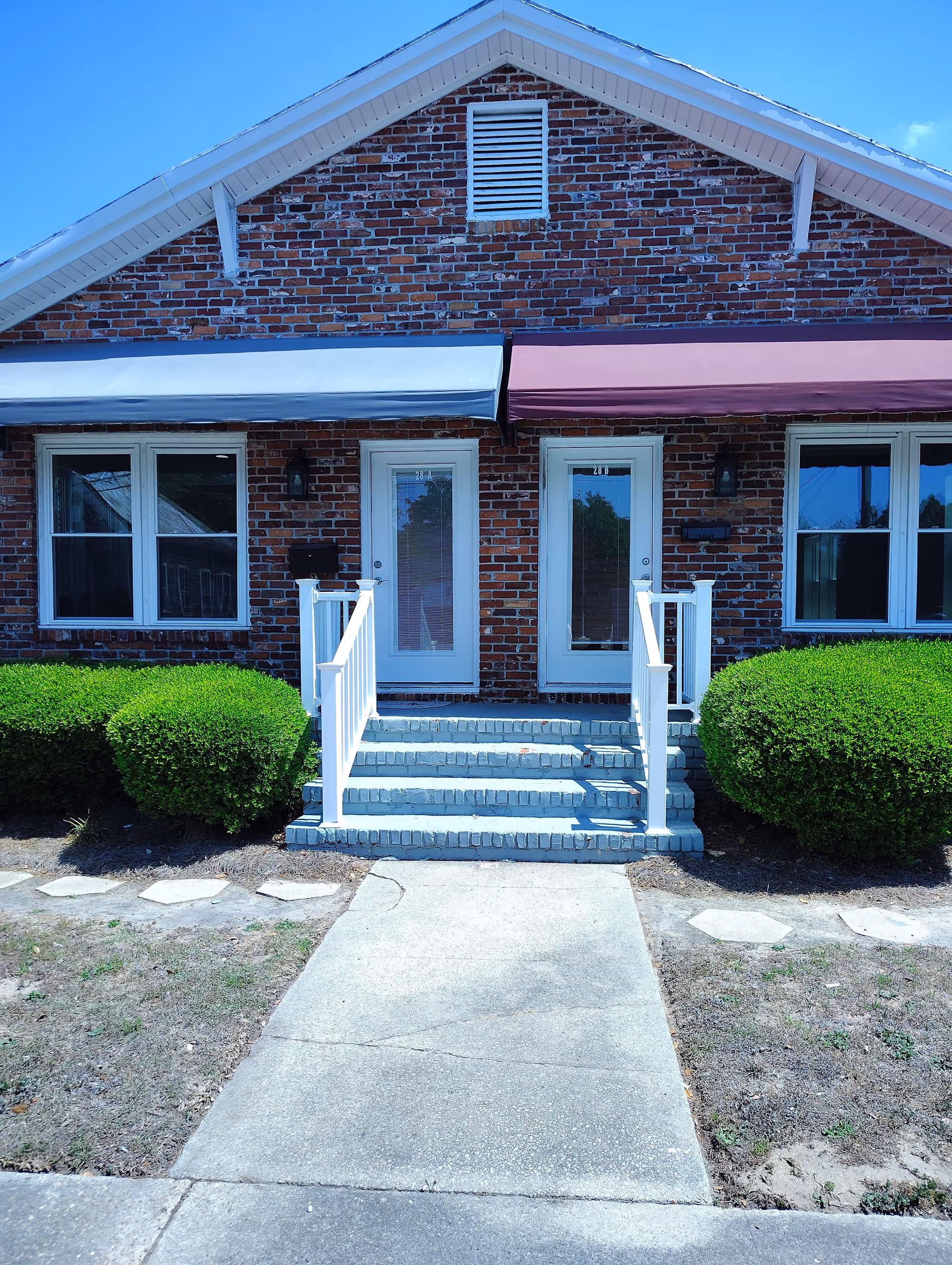 Brick facility exterior with white stairs, railings, double doors, and trimmed shrubs.