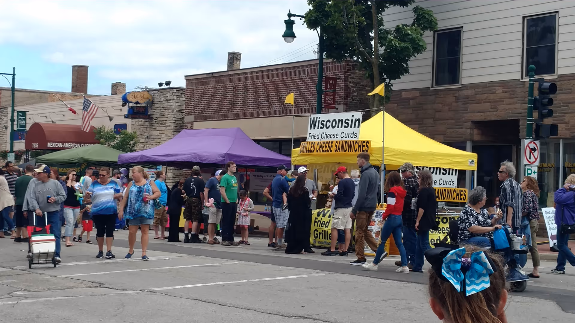 People walk past colorful vendor tents at an outdoor street fair.