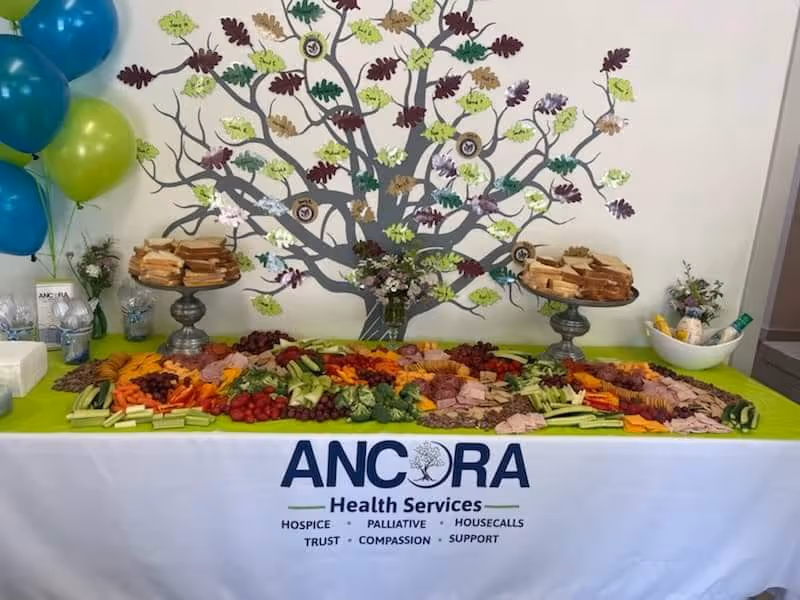 Colorful veggie and sandwich buffet on a lime-draped table with ANCORA Health Services backdrop.