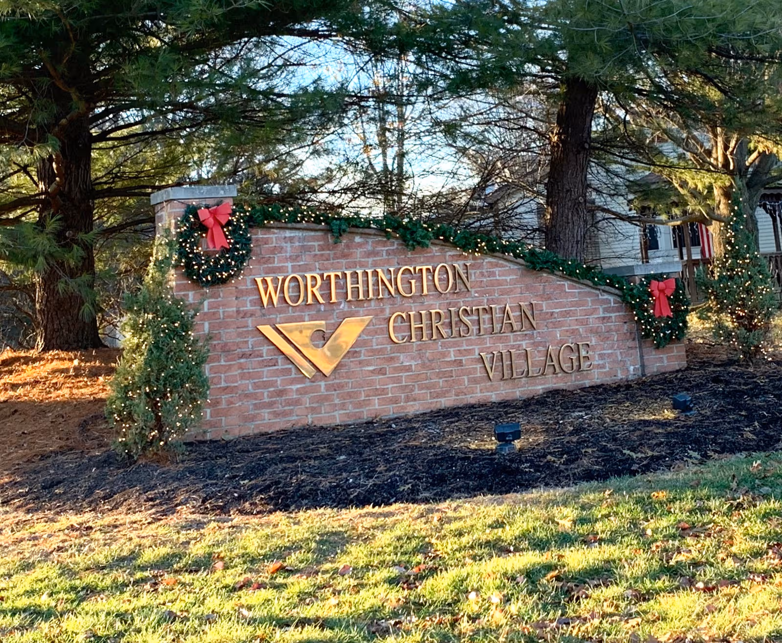Exterior brick sign reading Worthington Christian Village decorated with holiday garlands.