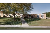 Single-story brick nursing facility with a lawn and trees in front.