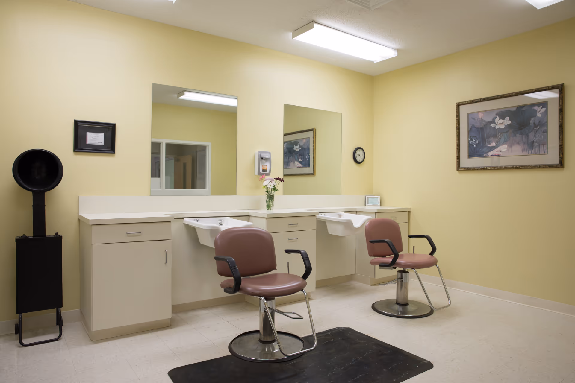 Interior of a senior living facility salon with two chairs, mirrors, sinks, and yellow walls.